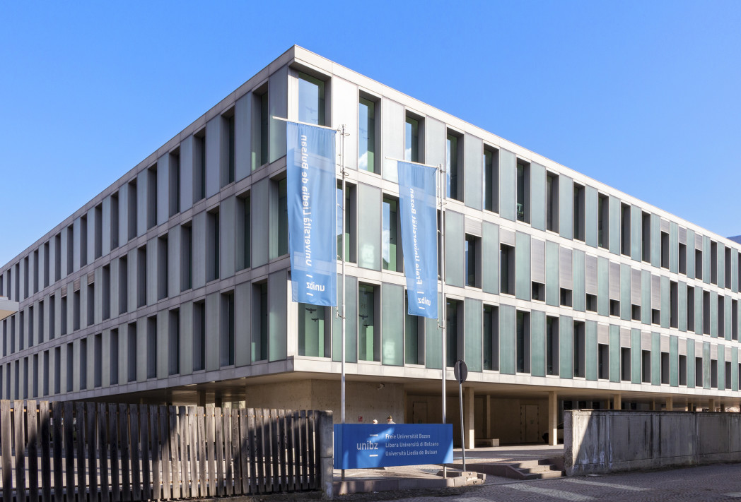 Edificio per uffici moderno a più piani, di forma rettangolare, con grandi finestre ed elementi verticali in facciata sotto un cielo azzurro limpido.