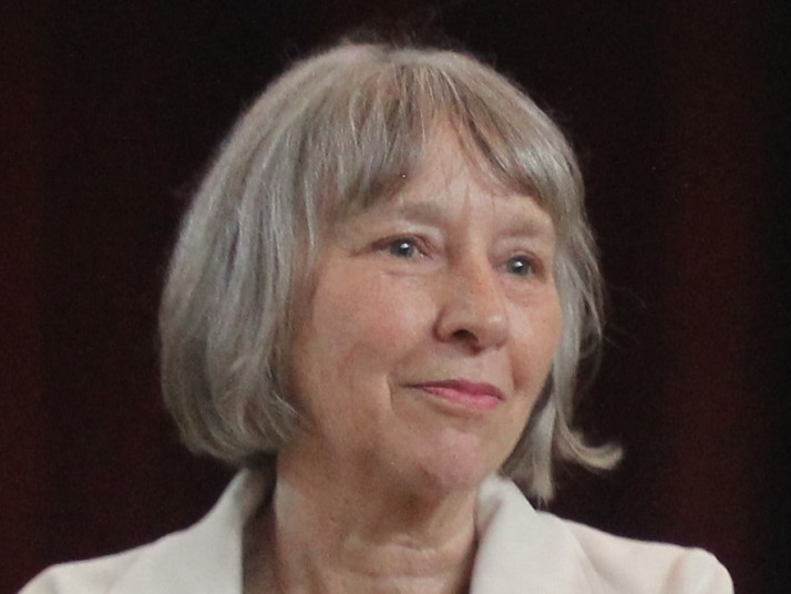 Eine Frau mit grauem Haar lächelt und schaut nach rechts.