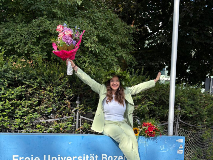 Eine junge Frau mit Blumen in den Händen, sitzt auf einer Mauer.