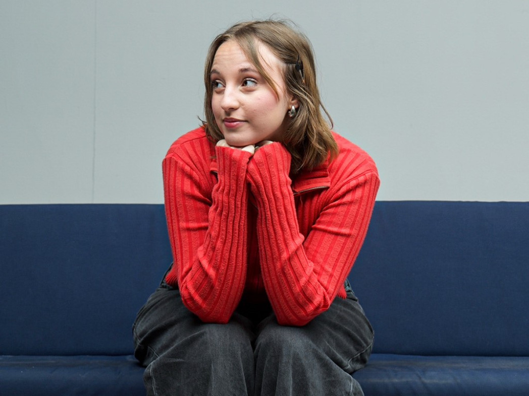 A young woman is seated on a bench and looking to the left. She laid her head on her hands.