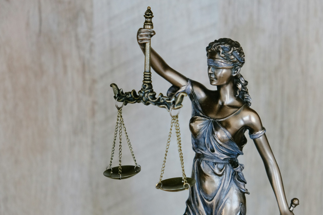 Statua bronzea della Giustizia, bendata e con una bilancia, su sfondo chiaro.