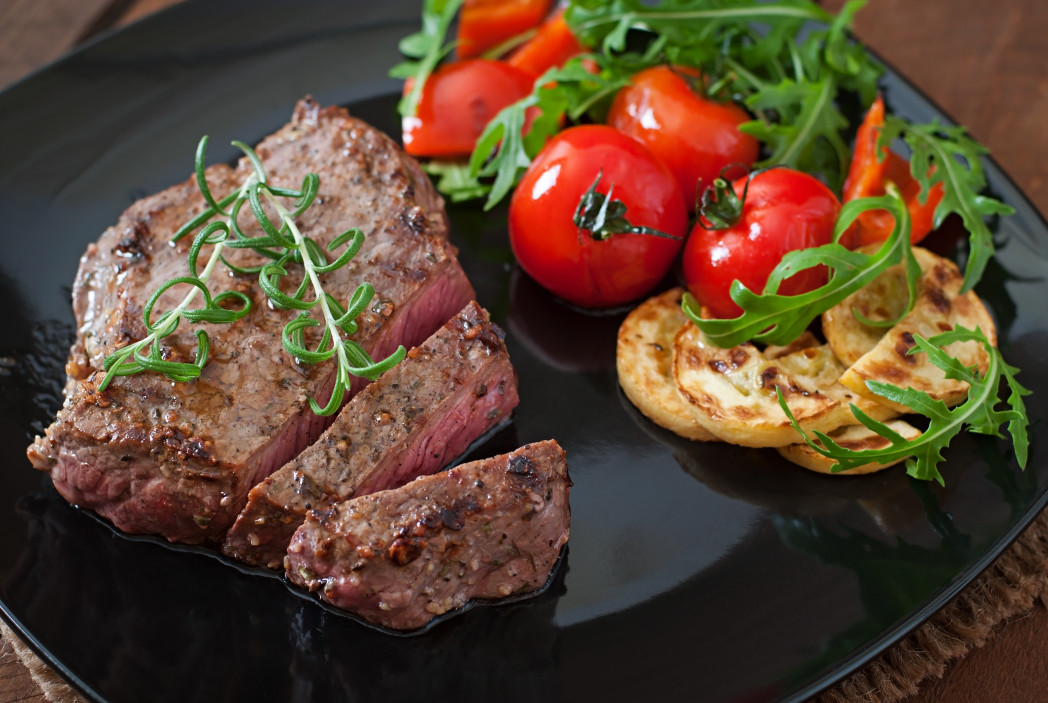 Teller mit einem Stück gebratenem Fleisch, garniert mit Gemüse (Tomaten, Rucola, Zucchini)