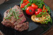 Teller mit einem Stück gebratenem Fleisch, garniert mit Gemüse (Tomaten, Rucola, Zucchini)