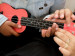 Vier Kinderhände auf einer Ukulele. Eine Kind zeigt dem anderen die Griffe.