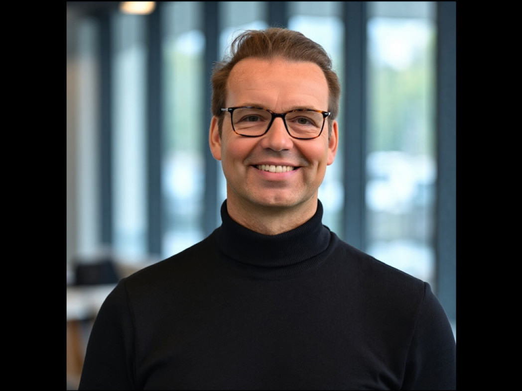Porträtfoto einer Person vor Glasfenstern mit Balken dazwischen.