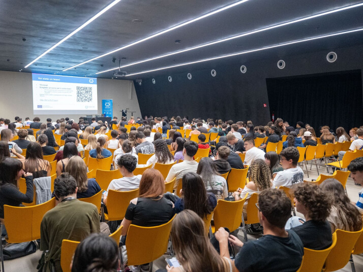 Aula magna piena di studenti durante una presentazione.