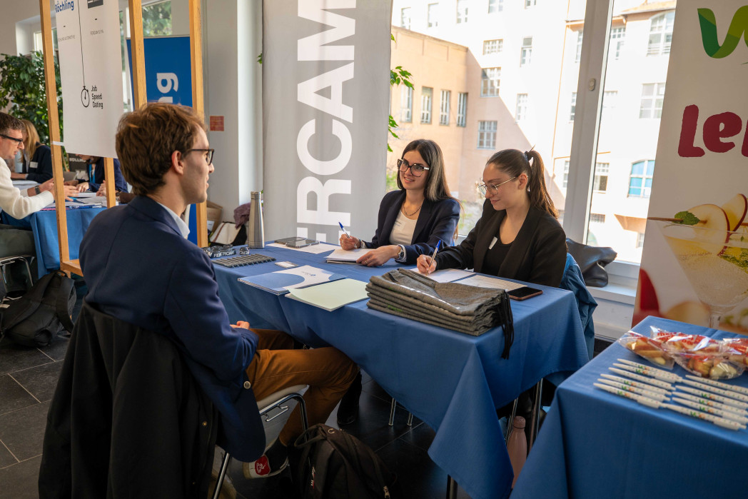 Due donne sedute a un tavolo conducono un colloquio con un uomo; prendono appunti mentre sul tavolo sono presenti materiali informativi.