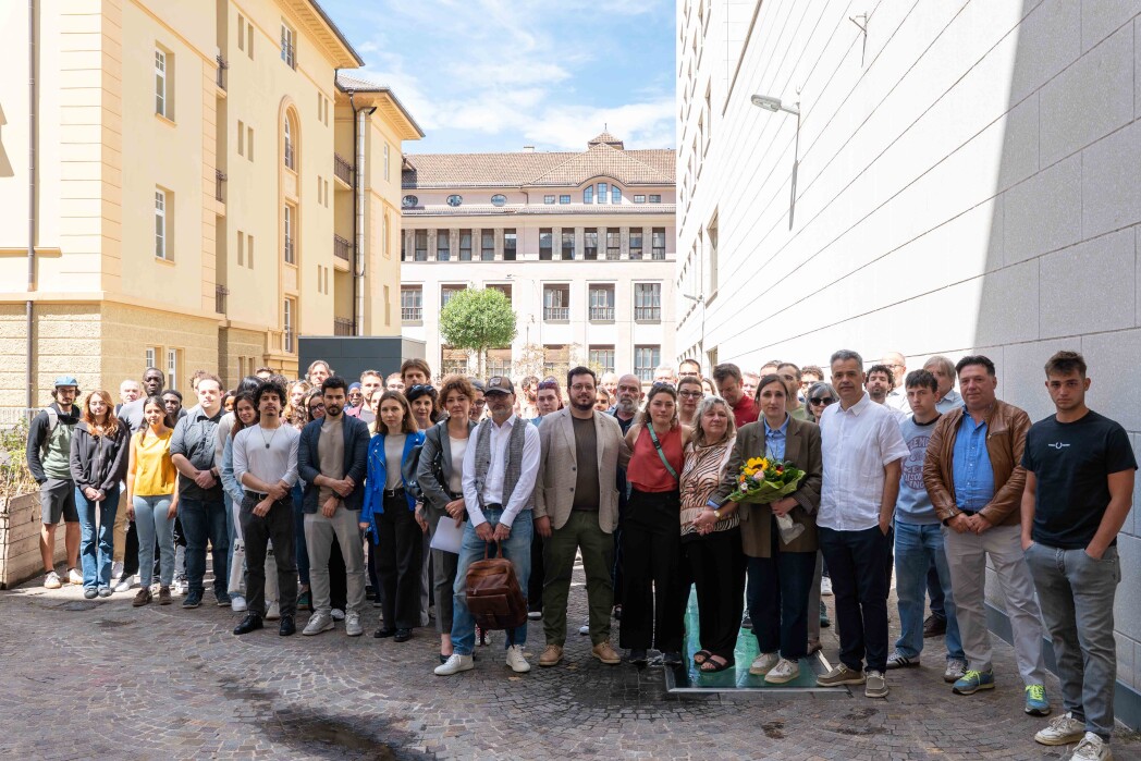 Grande gruppo di studenti e personale in posa in un cortile tra edifici universitari.