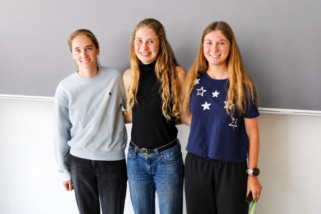 Tre giovani donne sorridono davanti a una lavagna.