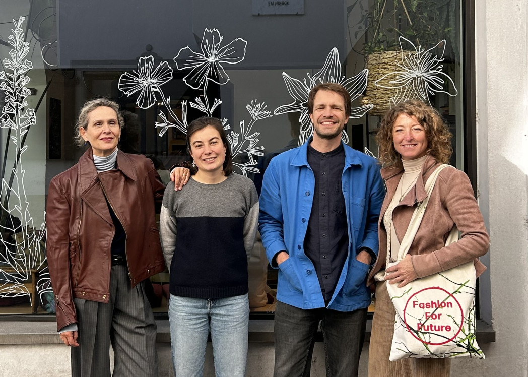 Vier Erwachsene stehen nebeneinander vor einem Schaufenster mit gezeichneten Blumenmotiven und lächeln in die Kamera.