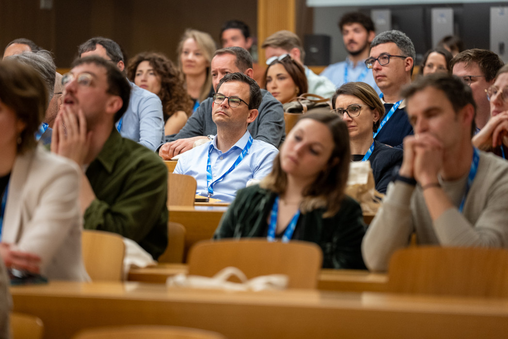 Pubblico adulto seduto in un’aula universitaria, ascolta con attenzione una conferenza.