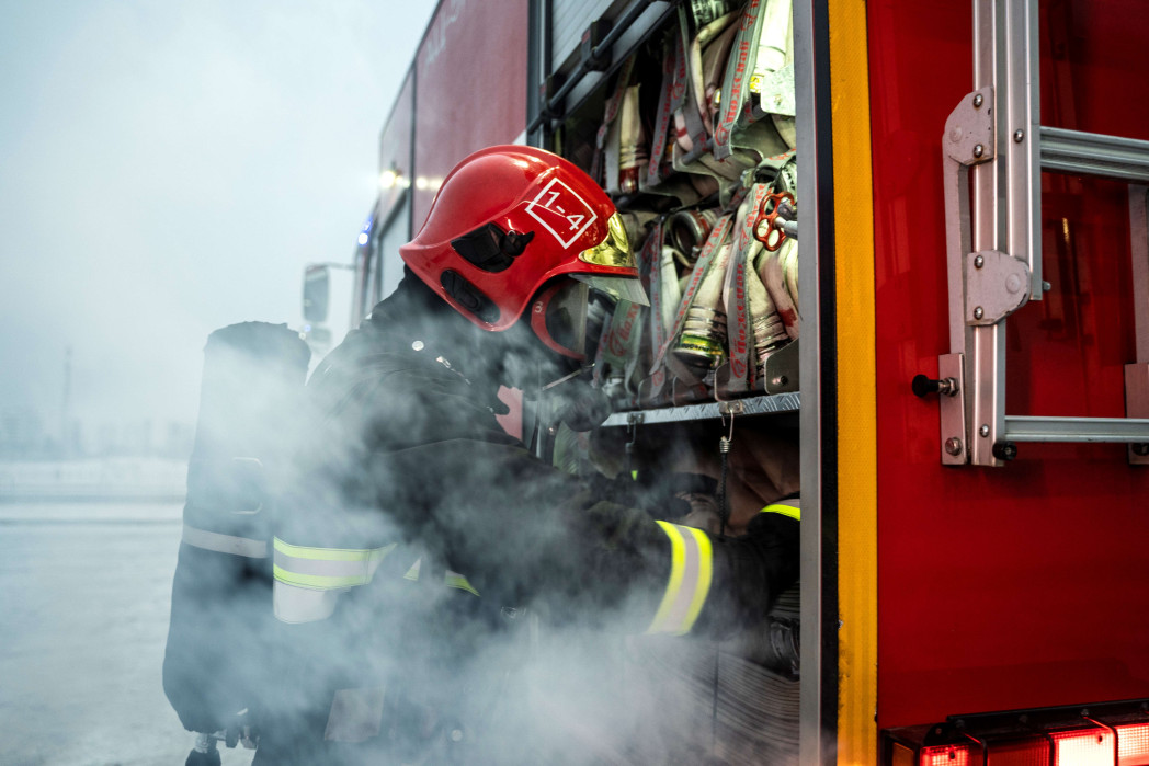 Un pompiere con indumenti protettivi e casco lavora su un veicolo dei soccorsi, circondato dal fumo