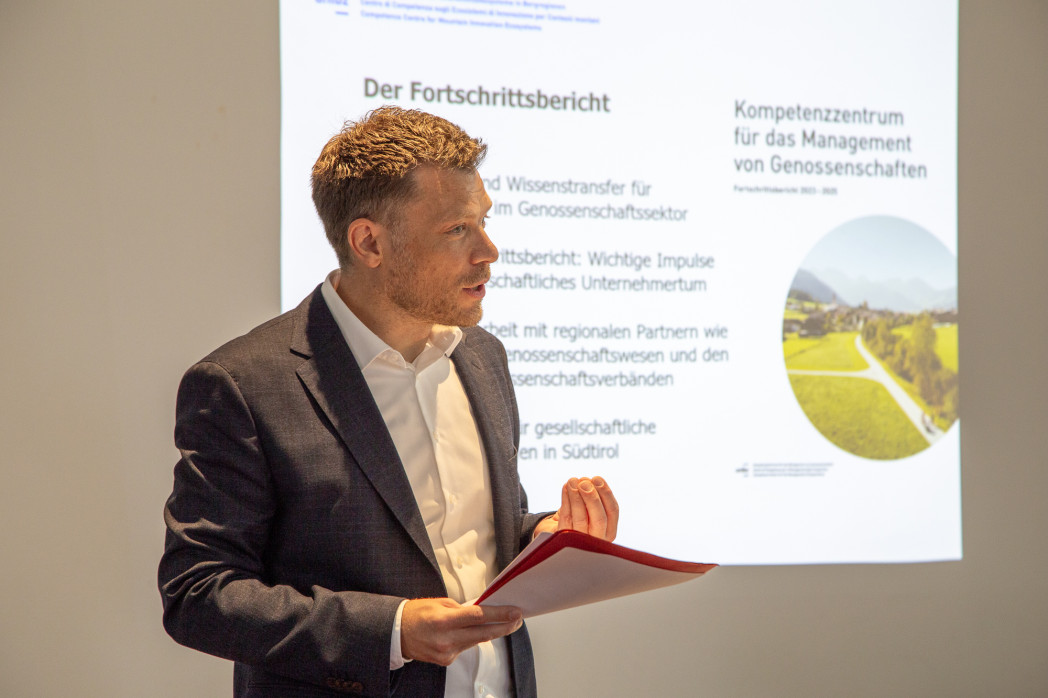 Mann bei einer Präsentation über Genossenschaften, mit rotem Hefter in der Hand.