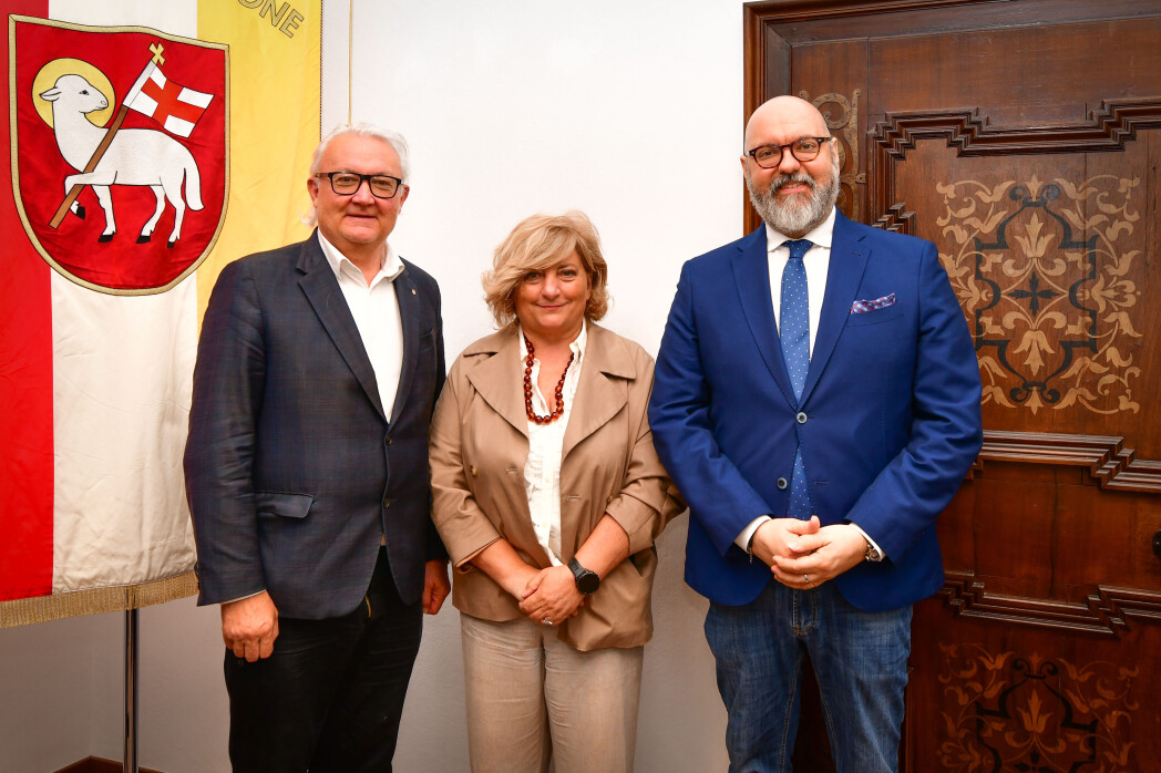 Drei Personen stehen bei einem Wappenbanner und einer verzierten Holztür.