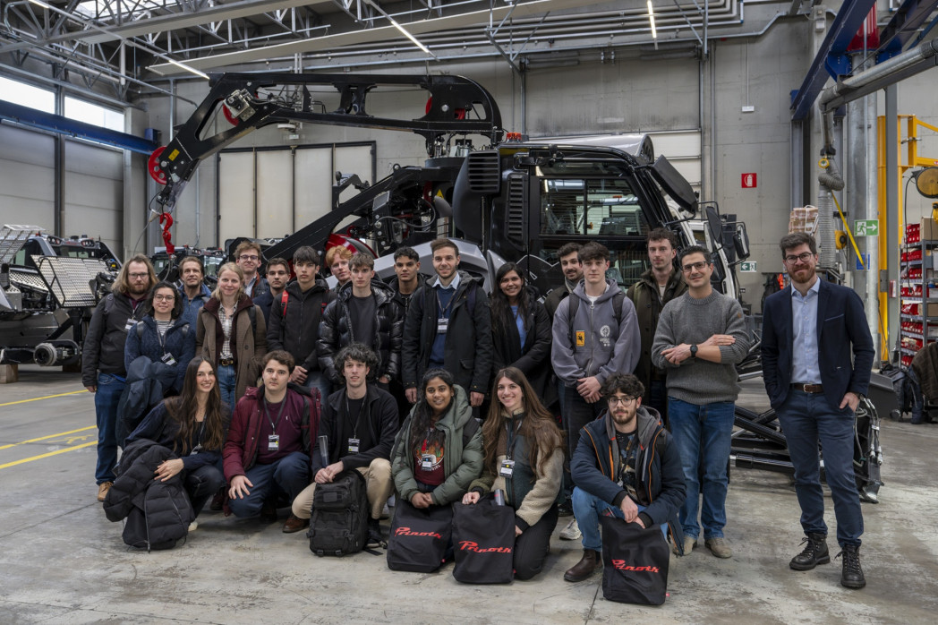 Gruppenfoto von etwa 20 Personen mit Namensschildern, die in einer Industriehalle vor einer Pistenraupe stehen und in die Kamera schauen.