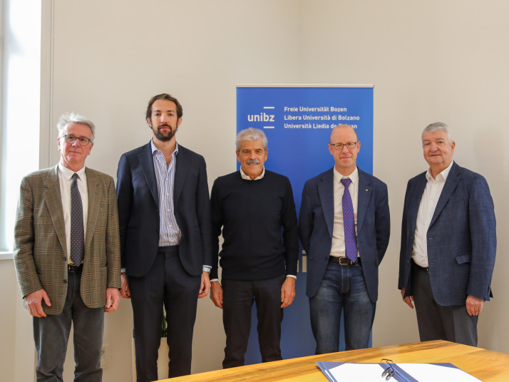 Fünf Männer in Geschäftskleidung stehen vor einem Banner der Freien Universität Bozen