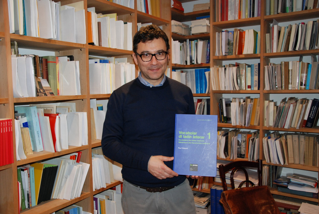 Bild einer Person, die die Publikation in Händen hält. Die Person steht von Bücherregalen.