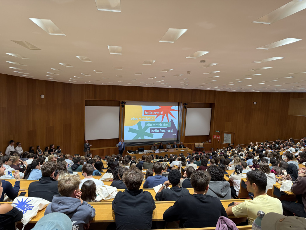 Un'aula universitaria ad anfiteatro gremita di studenti, focalizzati verso lo schermo durante una presentazione