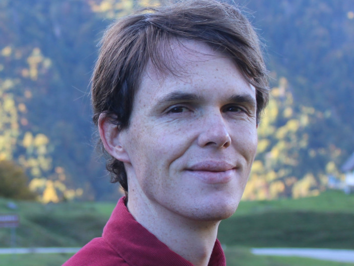 Portrait of a man outdoors with a forested mountain background.