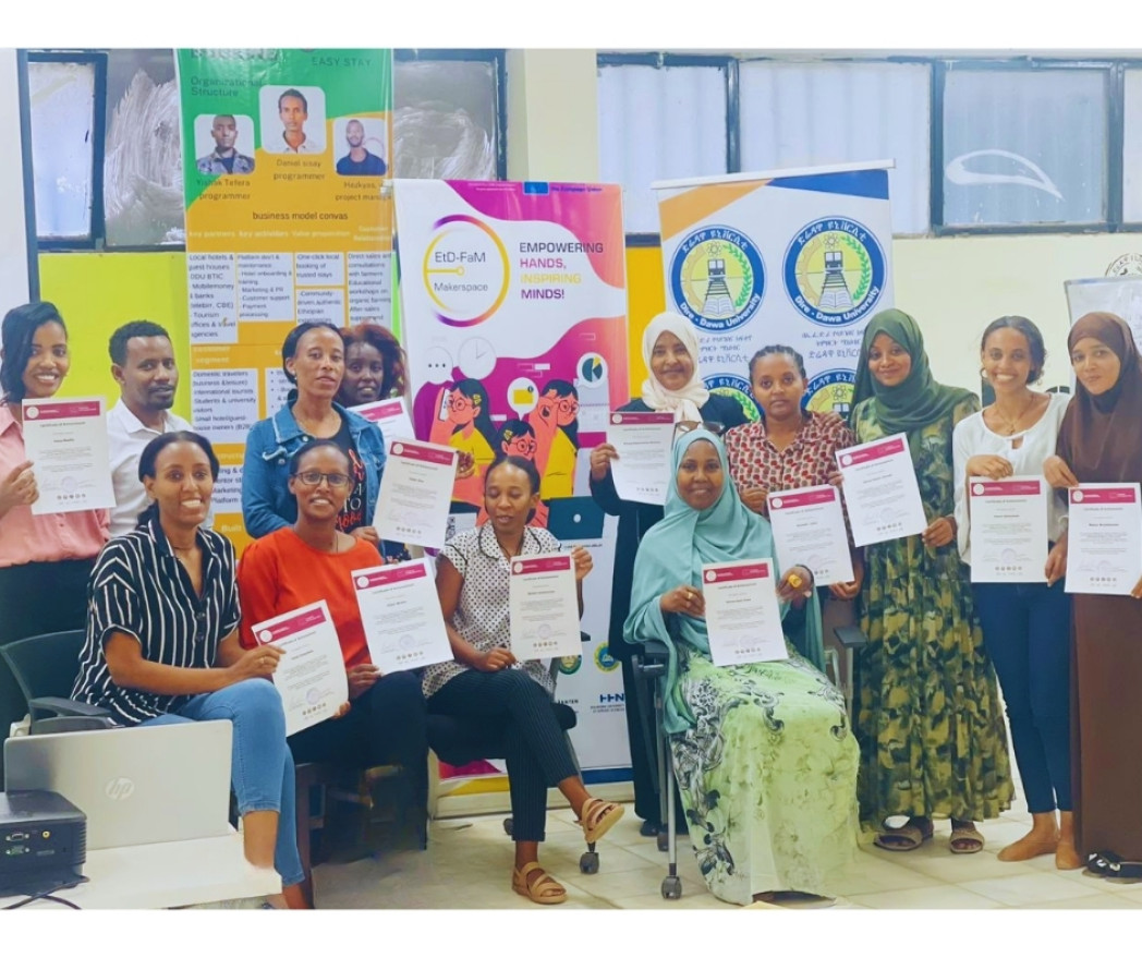 A group of around twenty people stands and kneels in front of a wall labeled “Maker Space,” holding certificates and posing together for a group photo.