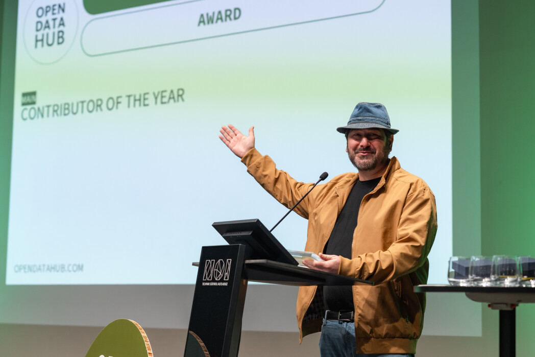 an gives an acceptance speech at an awards event in front of a projection screen.