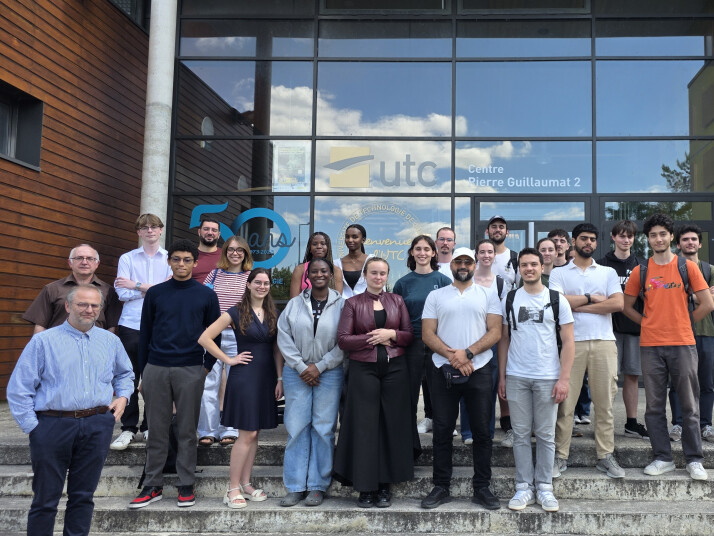 Group photo of students and staff standing on the steps in front of the glass entrance to UTC Centre Pierre Guillaumat 2.